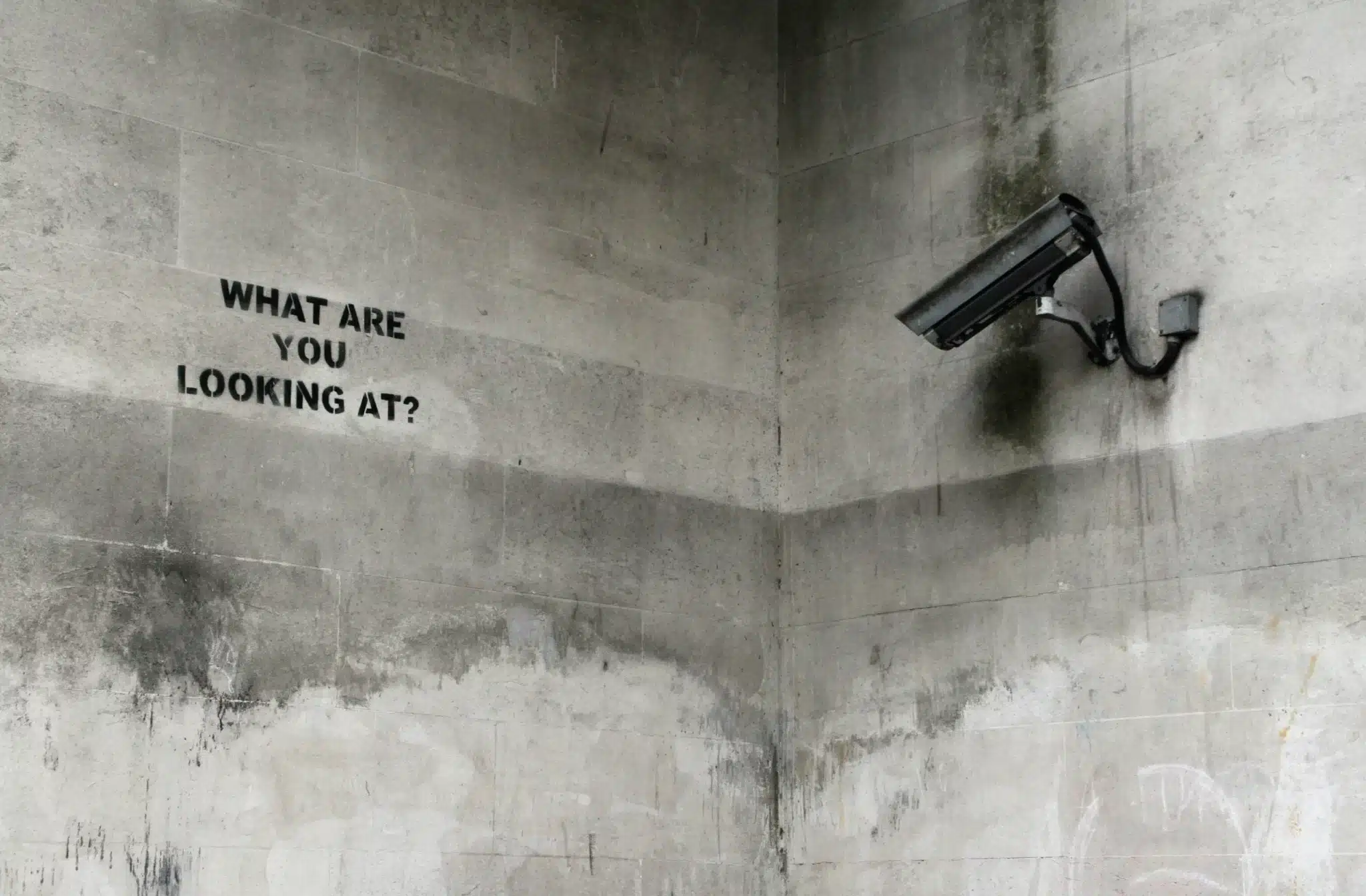 caméra de surveillance pointant vers une phrase inscrite sur un mur de béton